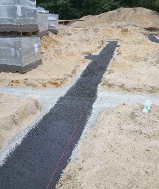 Wylewka z betonowej zaprawy na placu budowy, przygotowana do obsypki i dalszych prac fundamentowych, w otoczeniu piasku i materiałów budowlanych.